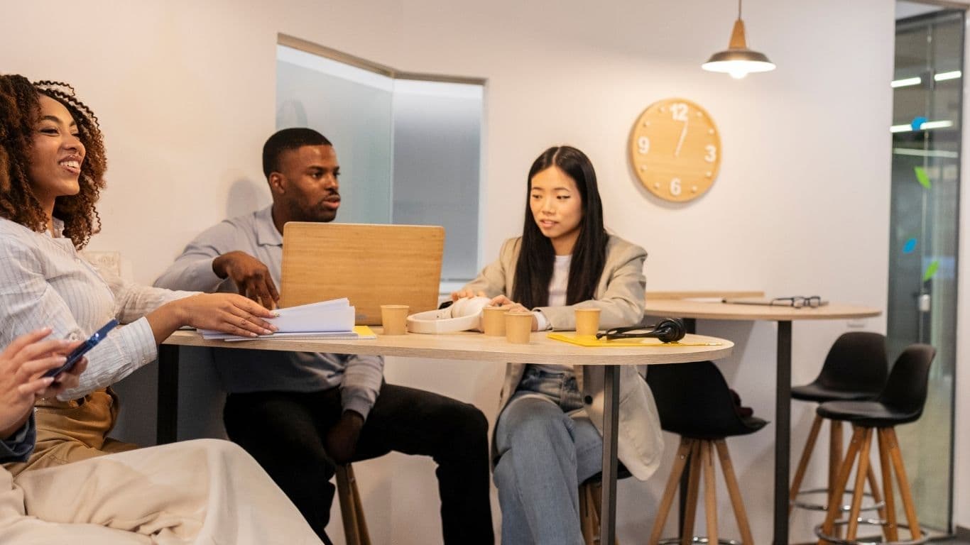Three diverse professionals collaborating at a table with laptops and coffee
